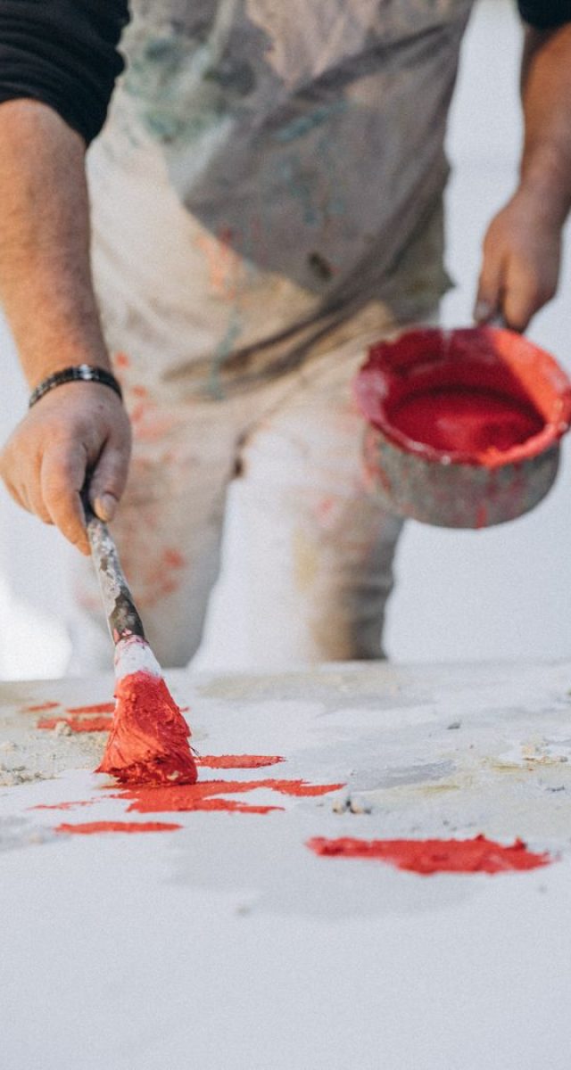 Close-up of an artist applying vibrant red paint on a canvas in a studio setting.